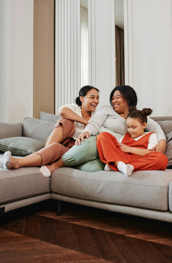 Two mothers sit on the couch with their child.