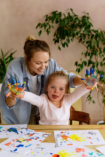 A mother and her child do fingerpainting while sitting at a table.