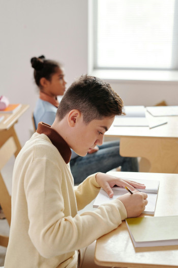 Students sit at their desks and write in their books.
