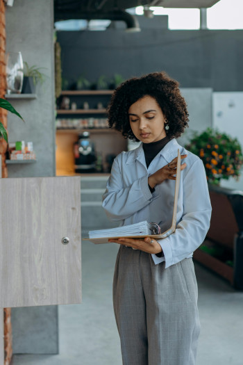 A woman stands in front of an open cabinet, holding an open ring binder full of papers.