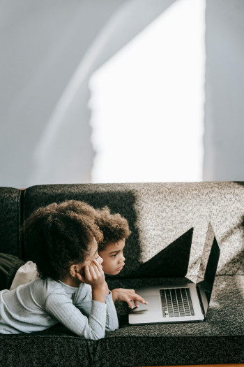 Two children lie on a couch, using a laptop.