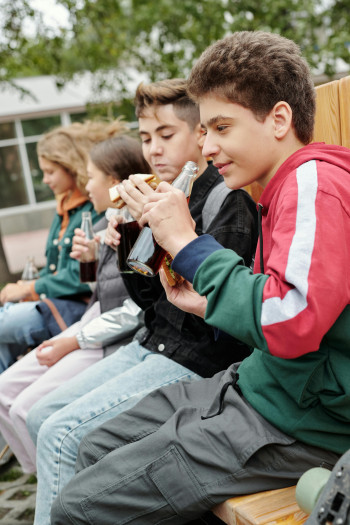 Four children sit in a line along a wooden bench, eating their lunch.