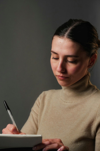 A woman with dark hair pulled back into a bun writes on a pad of paper.