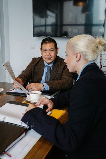 A man passes papers to a woman while they sit at a table holding a meeting.