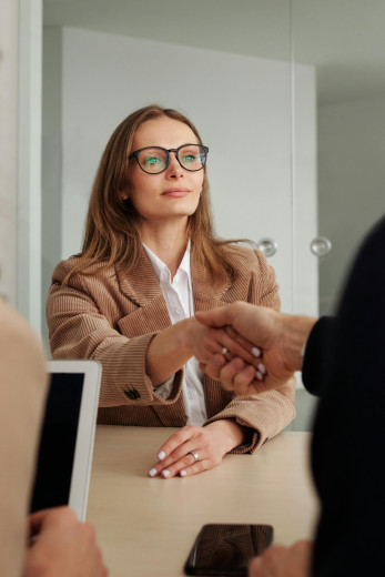 A woman with blonde hair shakes the hand of someone sitting across the table from her.