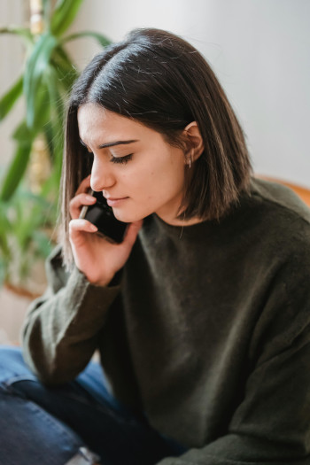 A woman with brown hair holds a phone to her ear as though on a call.