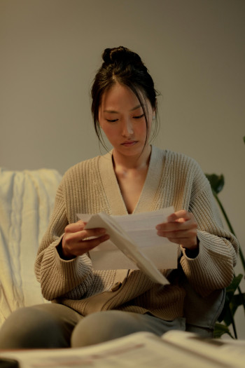 A woman sits on a couch and reads a letter.