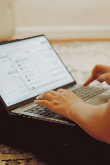 A person's hands can be seen as they type on their laptop's keyboard.