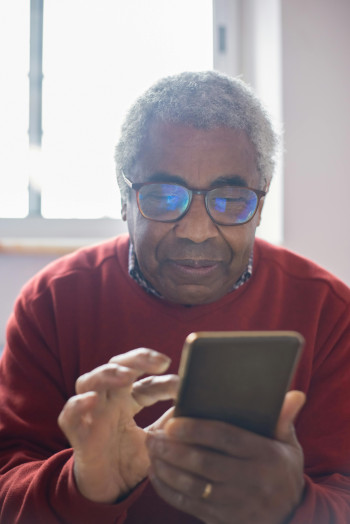 An elderly black man wearing glasses is tapping the screen of his phone.