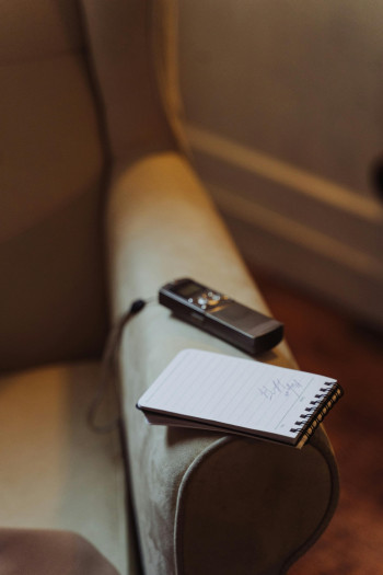 A recording device and a notebook sit on the arm of a couch.