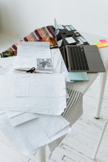 A laptop and papers cover the top of a desk. 