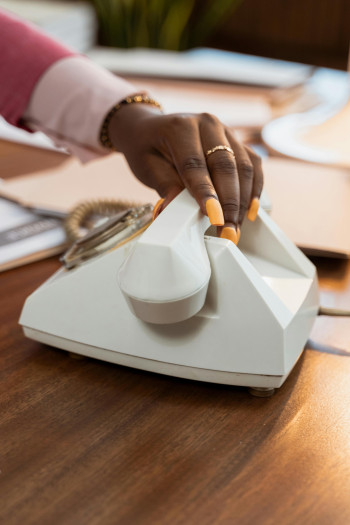 A black woman's hand, with painted nails, picks up a corded phone.