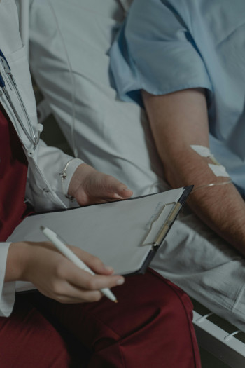 A patient lies in a hospital bed with a medical professional sitting next to them.