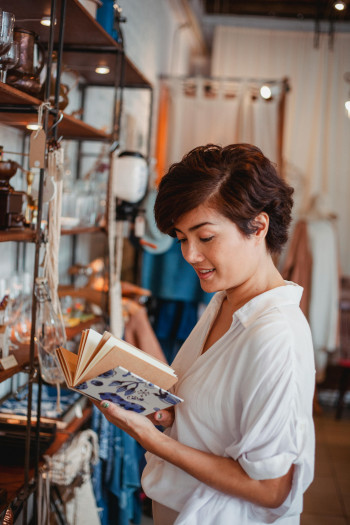 A woman with short, curly hair flips through a notebook while browsing in a retail store.