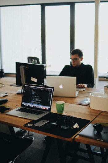 A man with short, dark hair sits on the far side of a desk full of computers and laptops.