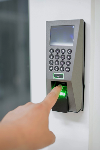 A person's finger rests on a fingerprint scanner below a number pad. The scanner has lit up green.