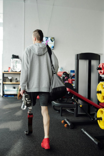 A man with a prosthetic leg carries a gym bag as he walks into a gym.